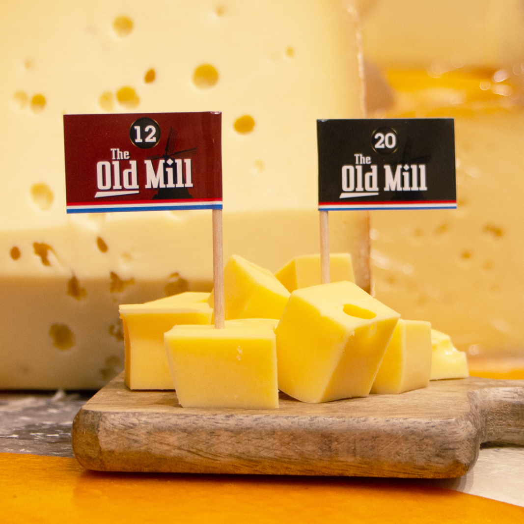 Portionsfähnchen mit Logodruck in Käsewürfeln auf einem Holzbrett.