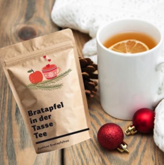 Bratapfeltee in brauner Tüte mit Teebecher und Weihnachtskugeln.