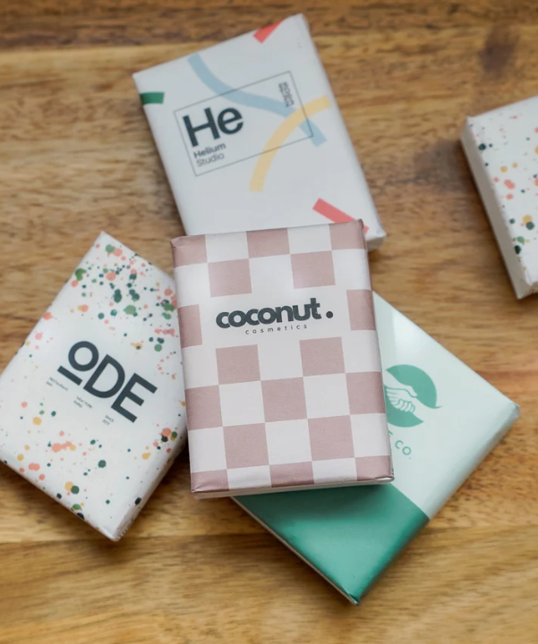 Fünf bedruckte Papiertaschentücher mit Verpackung auf Holztisch.